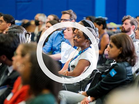 Participants of the 2023 HEAR Symposium are seated in a well-lit gymnasium smiling and watching a speaker at the front of the room out of view.